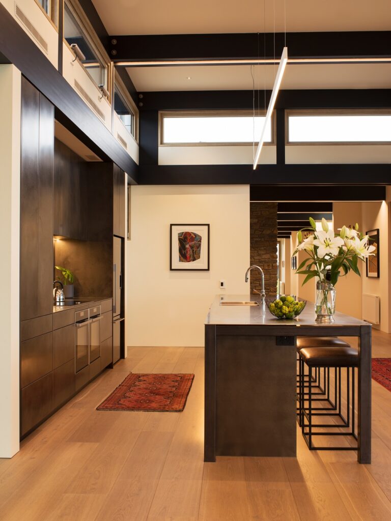 Metalier liquid metal smoky bronze finish on floor-to-ceiling kitchen cabinetry and a matching island in a modern open-plan home – New Zealand.