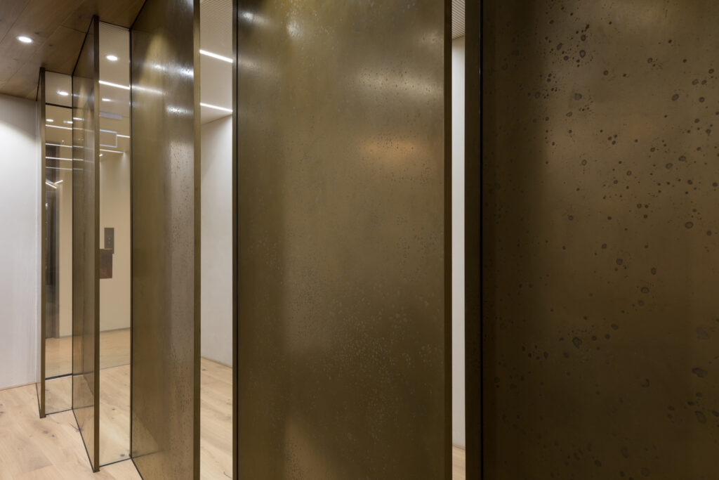 Textured bronze liquid metal wall panels in contemporary interior corridor with mirrored glass accents and recessed ceiling lighting – Dubai