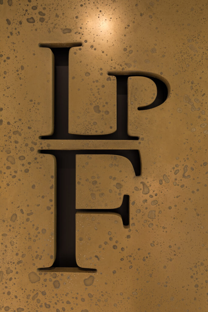 Brushed bronze metal plaque with embossed LPF monogram letters and textured patina finish – England