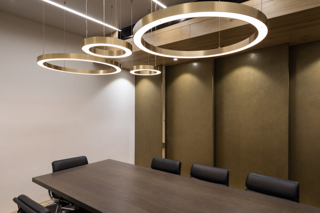 Modern conference room with dark wood table, black leather chairs, textured bronze wall panels, and circular pendant LED lighting – Canada