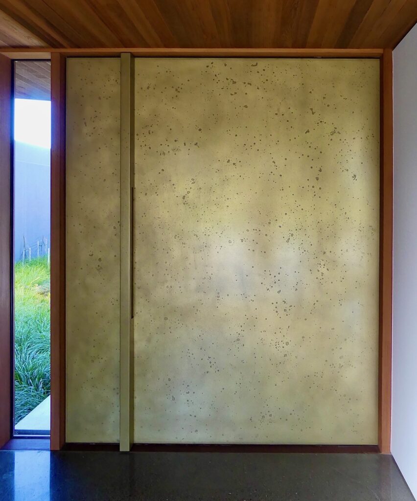 Custom brass front door with moonrock patina finish framed in timber, contemporary residential entry detail in Gloucester, England