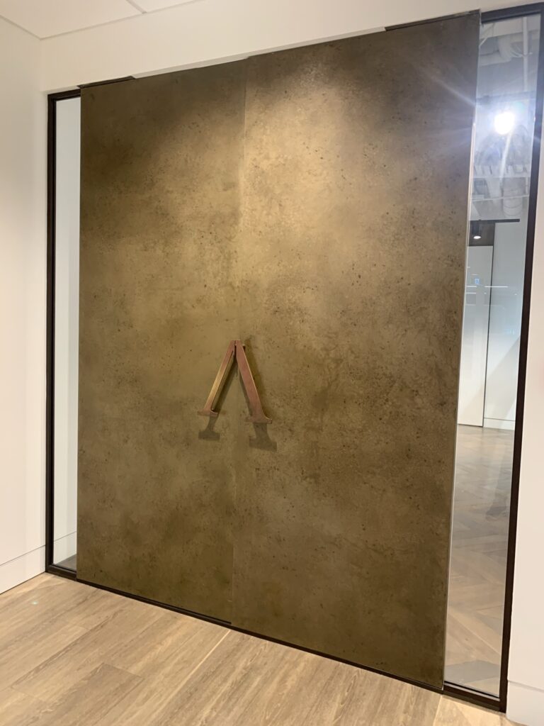 “Large sliding office entrance doors in heavily patinated brass with custom angular bronze handles, contemporary commercial interior - Gloucester, England
