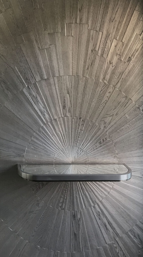 Radial timber wall installation with starburst pattern and floating metal shelf detail – bespoke interior feature wall in Dubai.