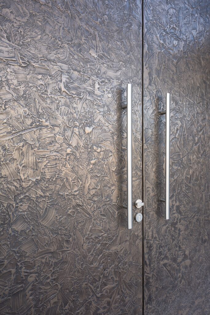 “Close-up of double entry doors in smoky bronze with heavily textured sculpted metal surface and sleek stainless steel vertical handles - Sittard, Netherland