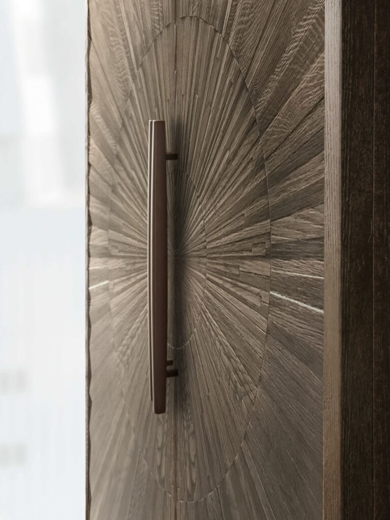 “Close-up of bespoke timber wardrobe door featuring radial starburst veneer pattern with bronze vertical handle – luxury interior joinery detail in England.