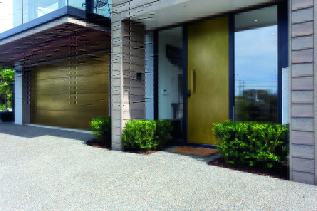 “Contemporary residential facade featuring custom brass front door and matching brass garage door, framed by timber cladding – modern home exterior in Brisbane, Australia